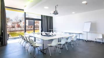 Una sala de conferencias moderna con una gran mesa, sillas blancas, una pizarra y un proyector.