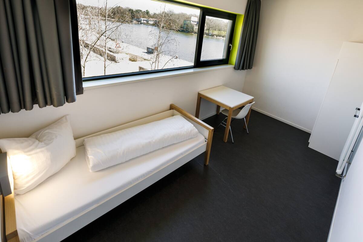 A small, modern room with a bed, a desk, and a chair.