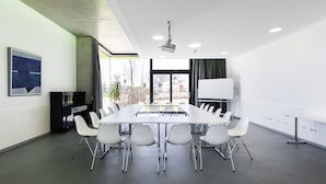 A conference room with a long table, white chairs, a piano, and a whiteboard. - Jugendherberge Schweinfurt - Hostel (Schweinfurt)