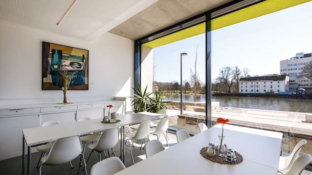 A modern meeting room with white tables and chairs, a large window with a yellow frame, and a painting on the wall. - Jugendherberge Schweinfurt - Hostel (Schweinfurt)