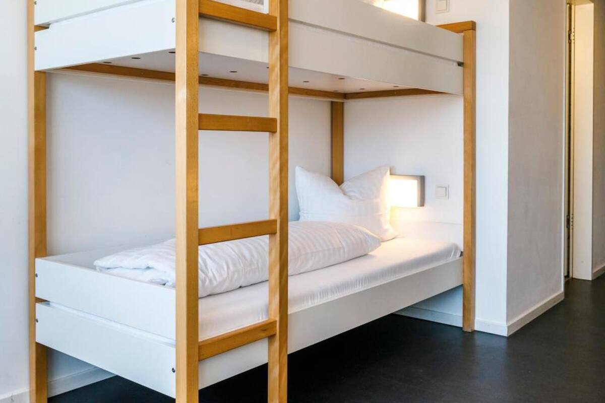 A bunk bed with wooden frames and white bedding in a room with a concrete ceiling and a blue accent wall.