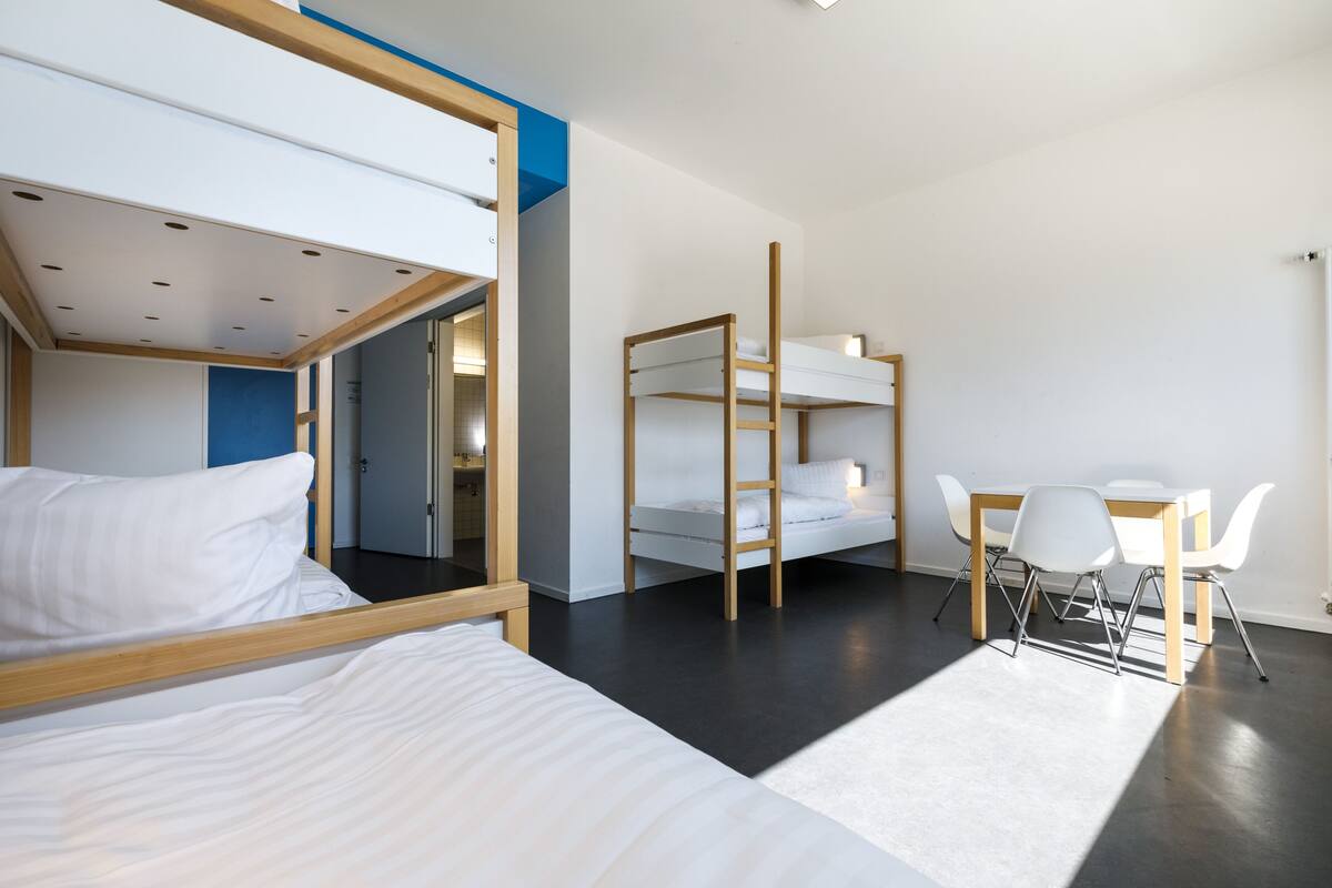 A modern hotel room with bunk beds, a desk, and chairs.