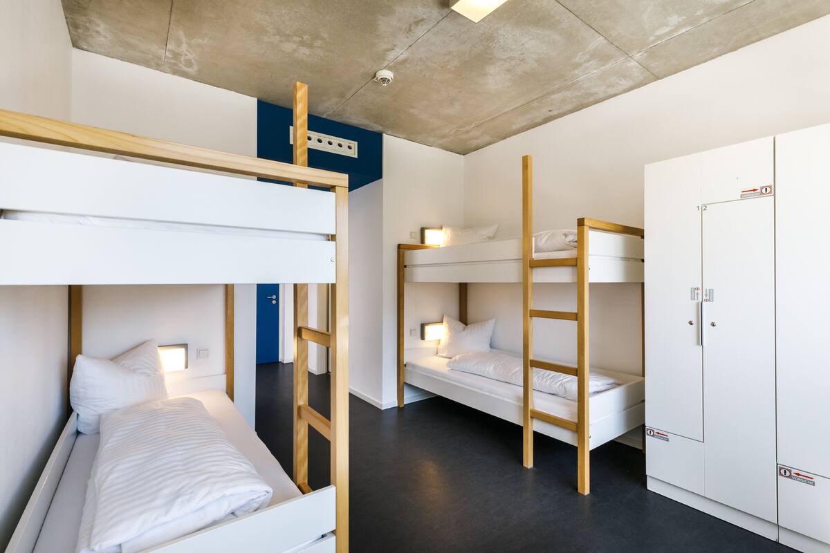 A dormitory room with bunk beds, a wardrobe, and a ceiling light fixture.