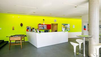Ein Empfangsbereich mit einer leuchtend grünen Wand, einem Empfangstresen, einer Uhr und einem Tischfußballtisch.