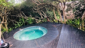 Un jacuzzi rodeado de una terraza de madera y abundante vegetación.