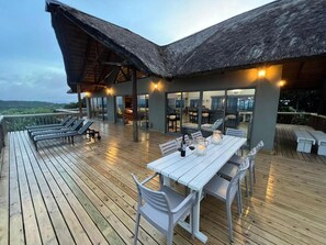 Une terrasse extérieure avec une table et des chaises, une structure dotée d’un toit de chaume et une vue sur le paysage.