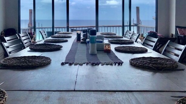 Un comedor con una mesa larga, sillas y vistas al mar a través de amplios ventanales.