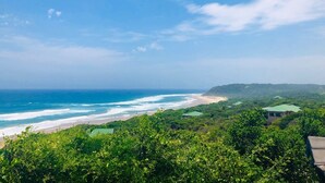 Paisaje costero con playa, océano y colinas boscosas.