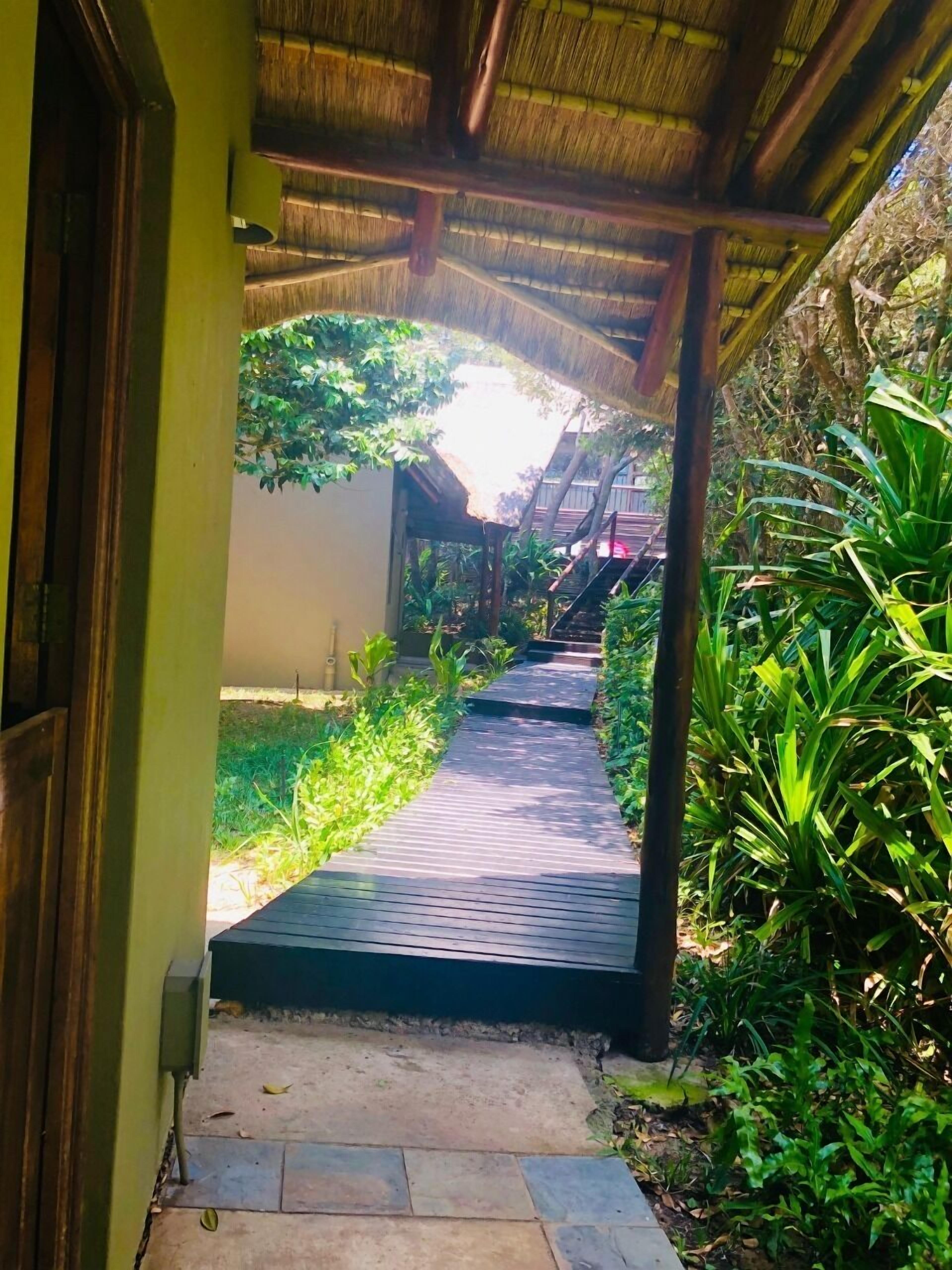 A pathway leading to a building with a thatched roof, surrounded by lush greenery.