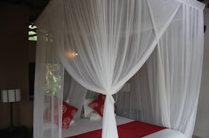 Un lit à baldaquin blanc agrémenté de touches de rouge, une table de chevet avec une lampe et une fenêtre donnant sur un paysage verdoyant.