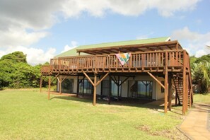 A wooden structure with a green roof and a balcony, surrounded by a grassy area and trees. - Kangela 1 (Ponta d'Ouro)