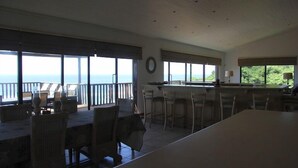 A spacious dining area with large windows overlooking the sea, a kitchen area with bar stools, and a view of the ocean. - Kangela 1 (Ponta d'Ouro)