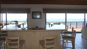 A bar area with a view of the sea, wooden chairs, and a framed picture on the wall. - Kangela 1 (Ponta d'Ouro)
