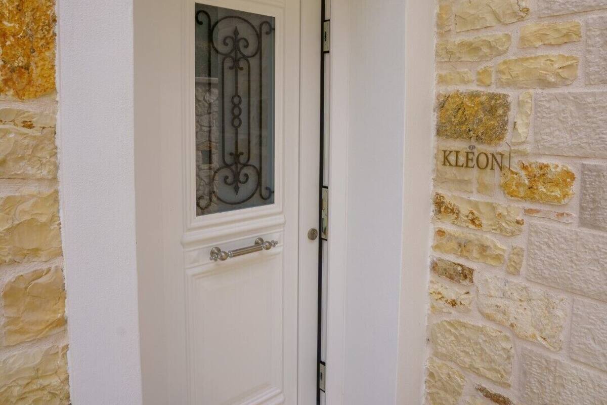 A white door with a glass panel and metal design, set in a stone wall with the name "KLEON" visible.