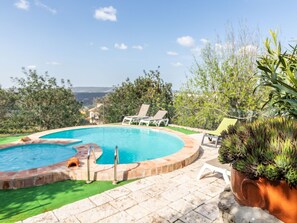 Relax by the pool surrounded by lush greenery and a scenic hilly view.