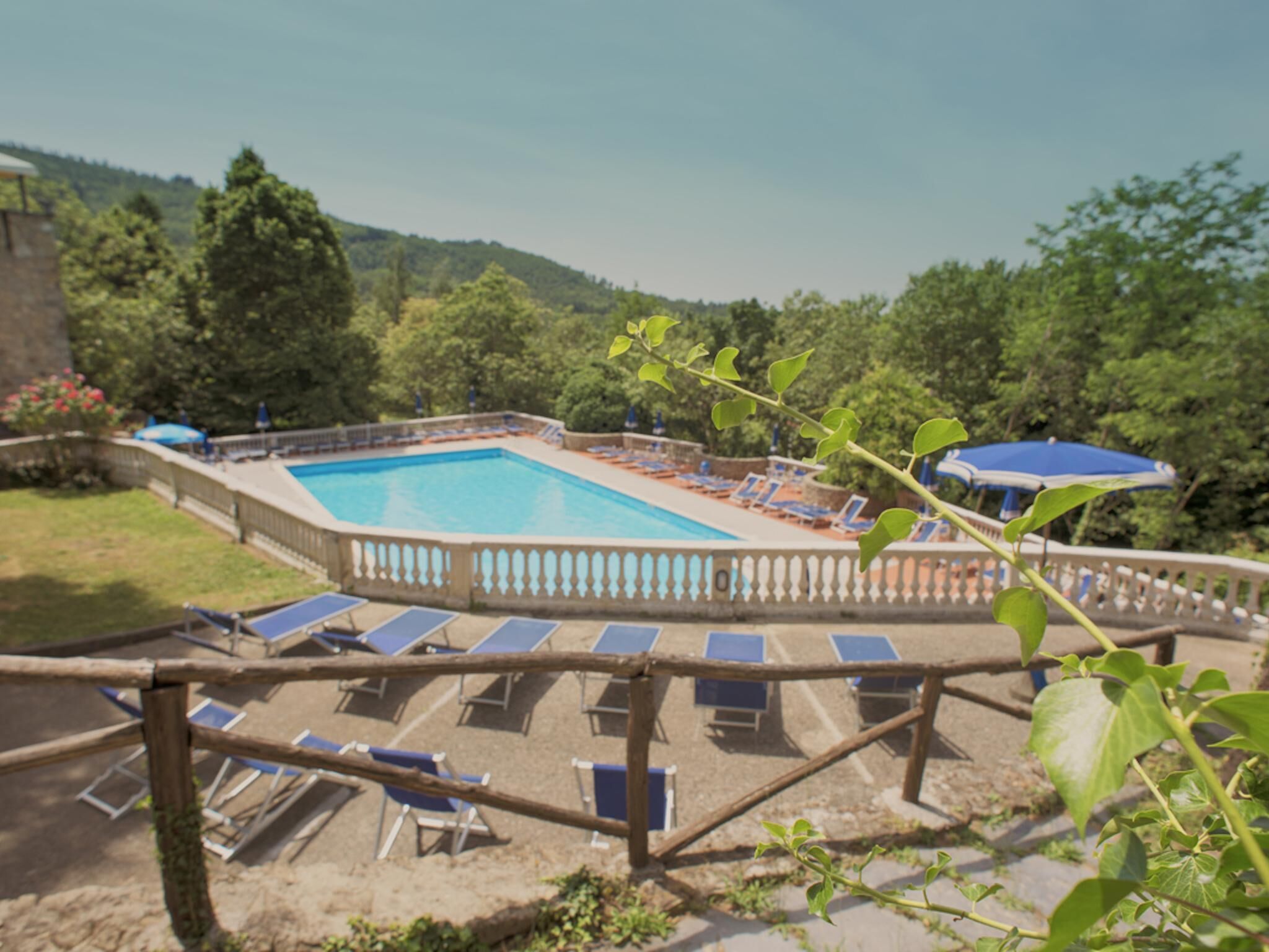 A swimming pool with lounge chairs and umbrellas, surrounded by greenery and hills.
