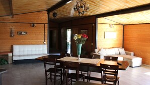 A wooden interior with a dining table, chairs, a white sofa, and a chandelier.