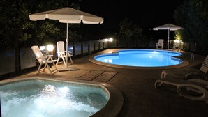 A swimming pool area with lounge chairs and umbrellas, surrounded by a fence and trees.