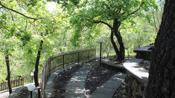 A stone pathway with a metal railing, surrounded by trees and a stone wall.