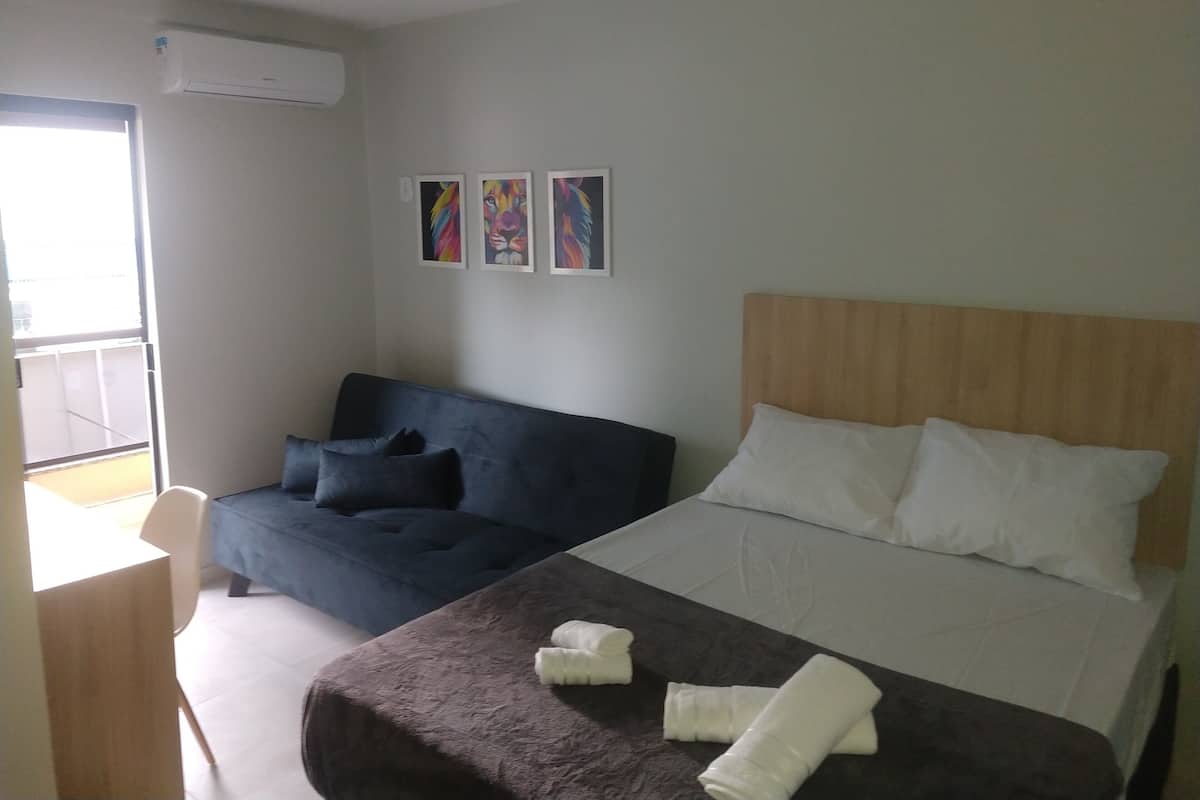 A hotel room with a bed, a sofa, a small table, and a chair. There are three paintings on the wall.