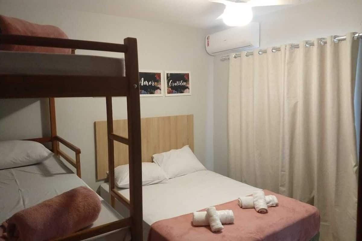 A bunk bed room with a wooden headboard, a single bed with a pink bedspread, and two framed pictures on the wall.