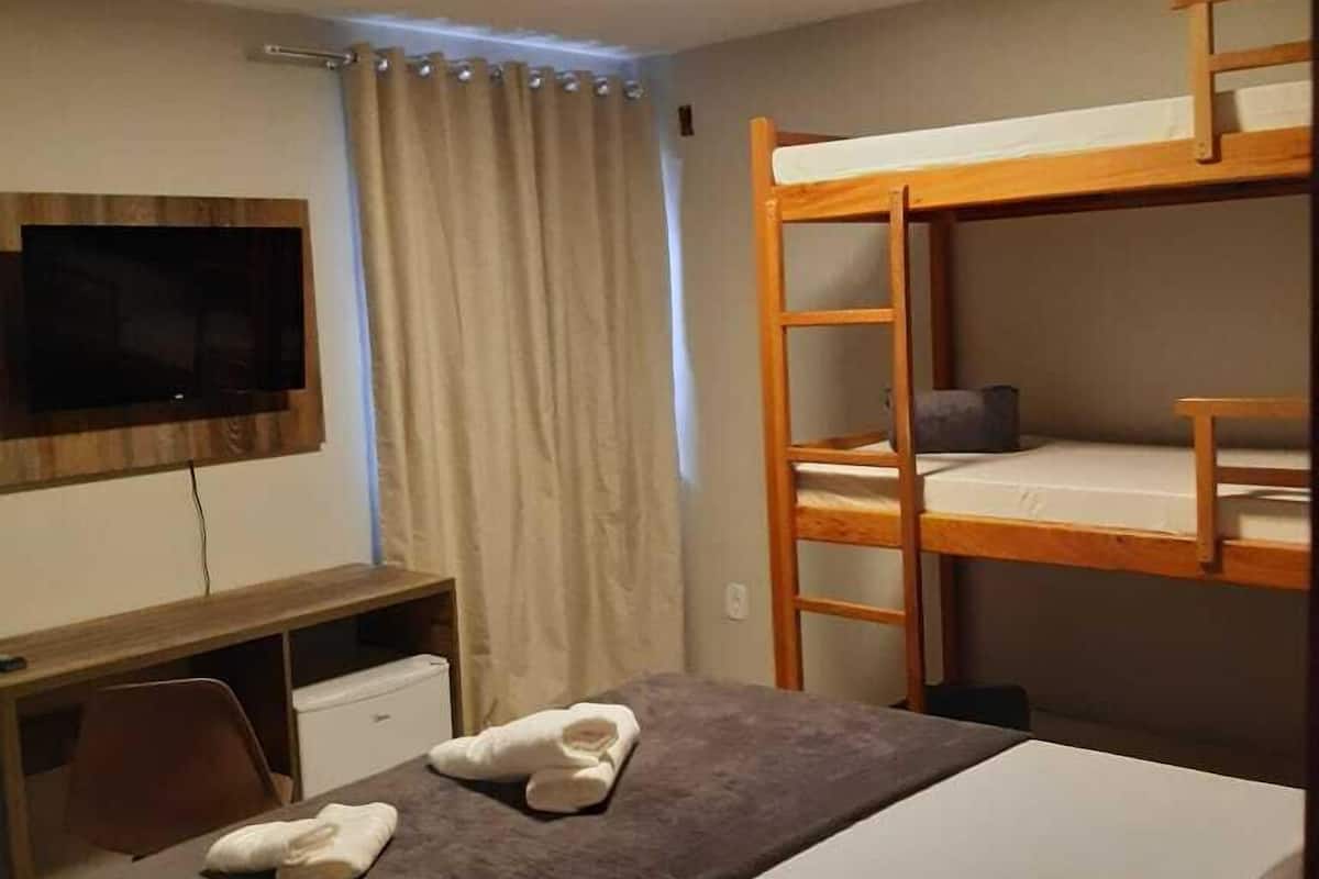 A hotel room with bunk beds, a desk, a television, and a window with curtains.