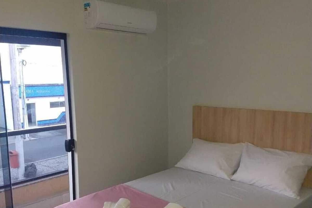 A hotel room with a bed, a ceiling fan, and a window with a view of a building outside.
