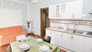 Een eethoek met een tafel voor vier personen, een keuken met witte kasten en een oranje bank.