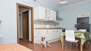 A compact kitchen with white cabinets, a dining table with a green tablecloth, and a dog sitting on the floor.