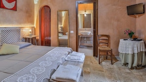 Ein Schlafzimmer mit Bett, Nachttisch, Stuhl, kleinem Tisch mit Vase und einem durchgegangenen Tür angedeuteten Badezimmer.