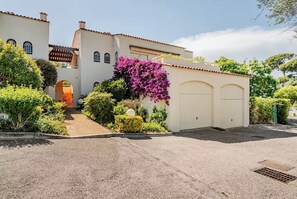 Ein zweigeschossiges Gebäude mit Auffahrt, Garage und einem gepflegten Garten mit verschiedenen Pflanzen und einem blühenden Busch in Lila.
