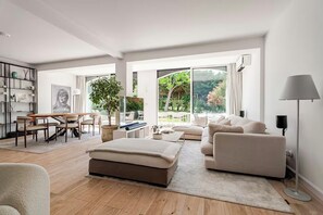 A spacious living room with a large window, a sofa, a coffee table, and a bookshelf.