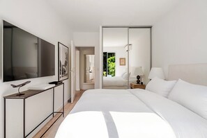 Habitación de hotel moderna con una cama grande, un escritorio, un televisor y una puerta corrediza que da a un balcón.