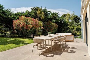 Eine Terrasse im Freien mit Tisch und Stühlen, umgeben von üppiger Bepflanzung und Bäumen.