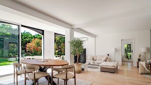 Una sala de estar moderna con comedor, un sofá, un televisor y un amplio ventanal con vistas a un jardín.