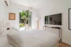 A bedroom with a bed, a TV, a lamp, and a sliding glass door to a garden.