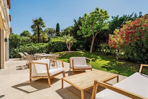 Eine Terrassensitzgruppe im Freien mit Lounge-Möbeln und Tisch, umgeben von Pflanzen und Bäumen.