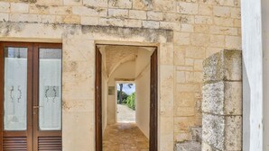 A narrow stone corridor leading to a door with a glass panel, flanked by stone walls and a wooden door.