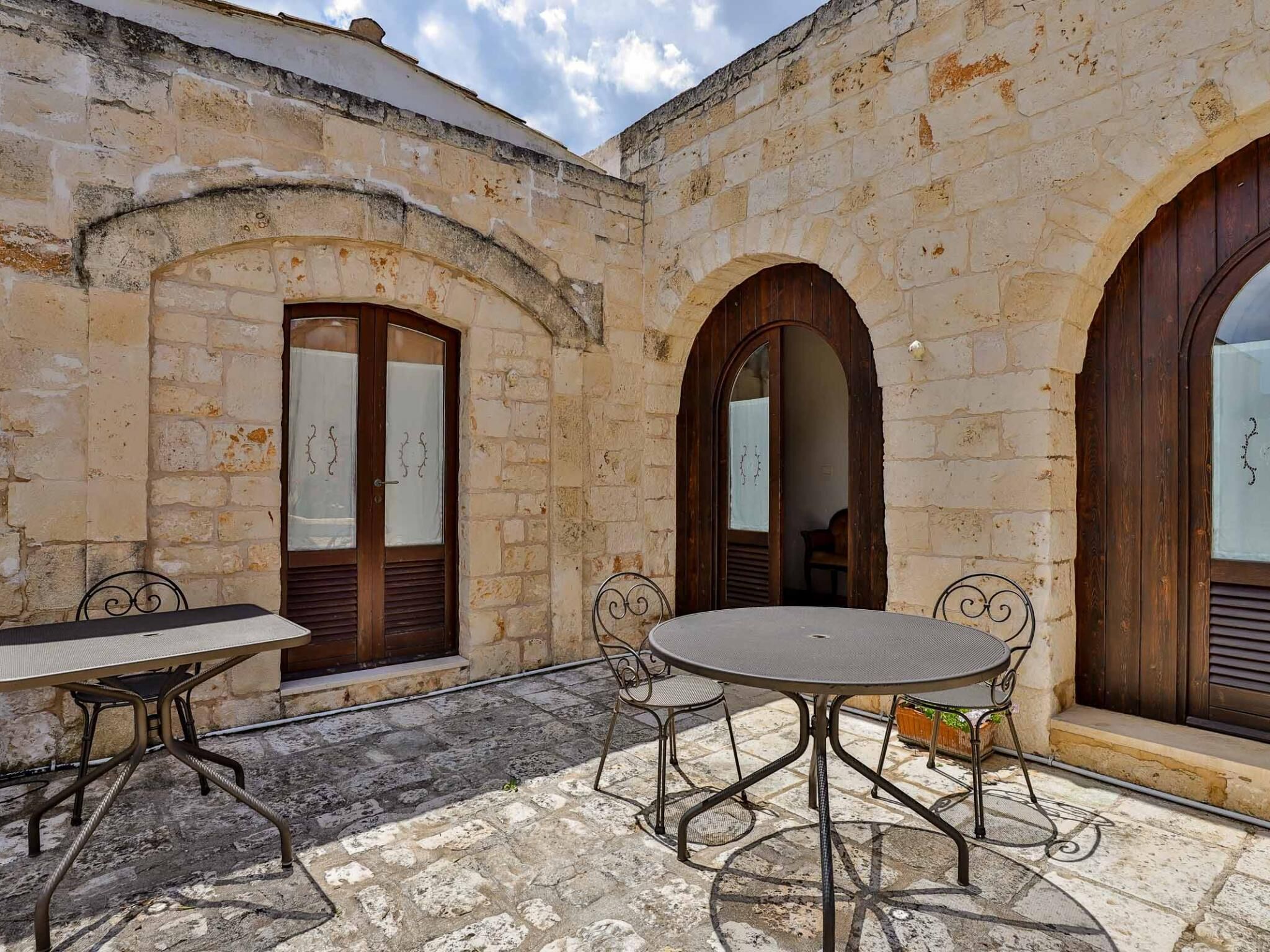 Une terrasse extérieure avec un sol en pierre, une table ronde, deux chaises et des portes en bois.