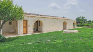 Un bâtiment en pierre avec un toit en tuiles, un patio couvert et une pelouse bien entretenue.