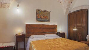 Une chambre à coucher avec un grand lit, une tête de lit en bois, une tapisserie, une armoire et une table de chevet avec une lampe.