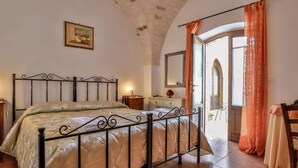 Ein Schlafzimmer mit Bett, Nachttisch, Kommode und Spiegel. Ein Fenster mit Vorhängen bietet einen Blick nach außen.