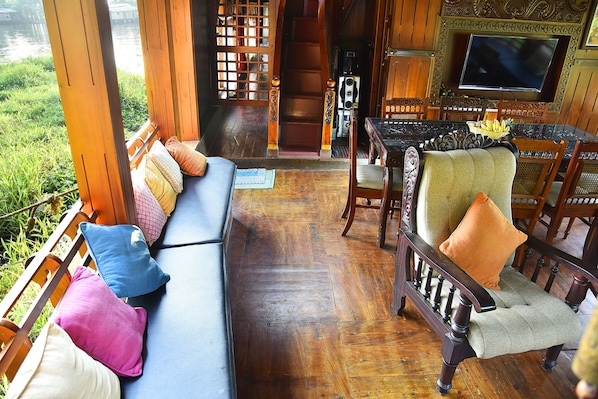 A wooden interior with a sofa, chairs, a dining table, and a television. - Premium Luxury Houseboat (Ambalapuzha)