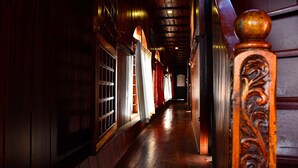 Un pasillo de madera con piso pulido, una barandilla decorativa y varios ventanales con cortinas.