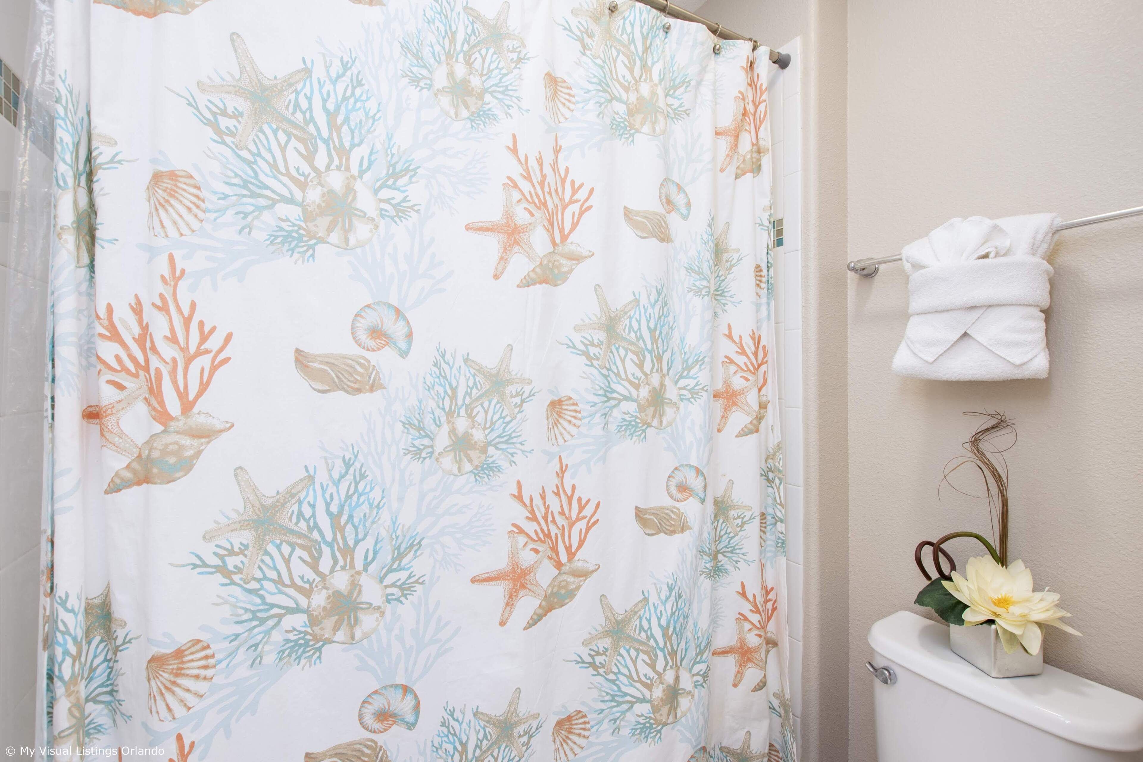 A bathroom with a shower curtain featuring a sea life pattern, a toilet with a flower decoration, and a towel rack with a folded towel.