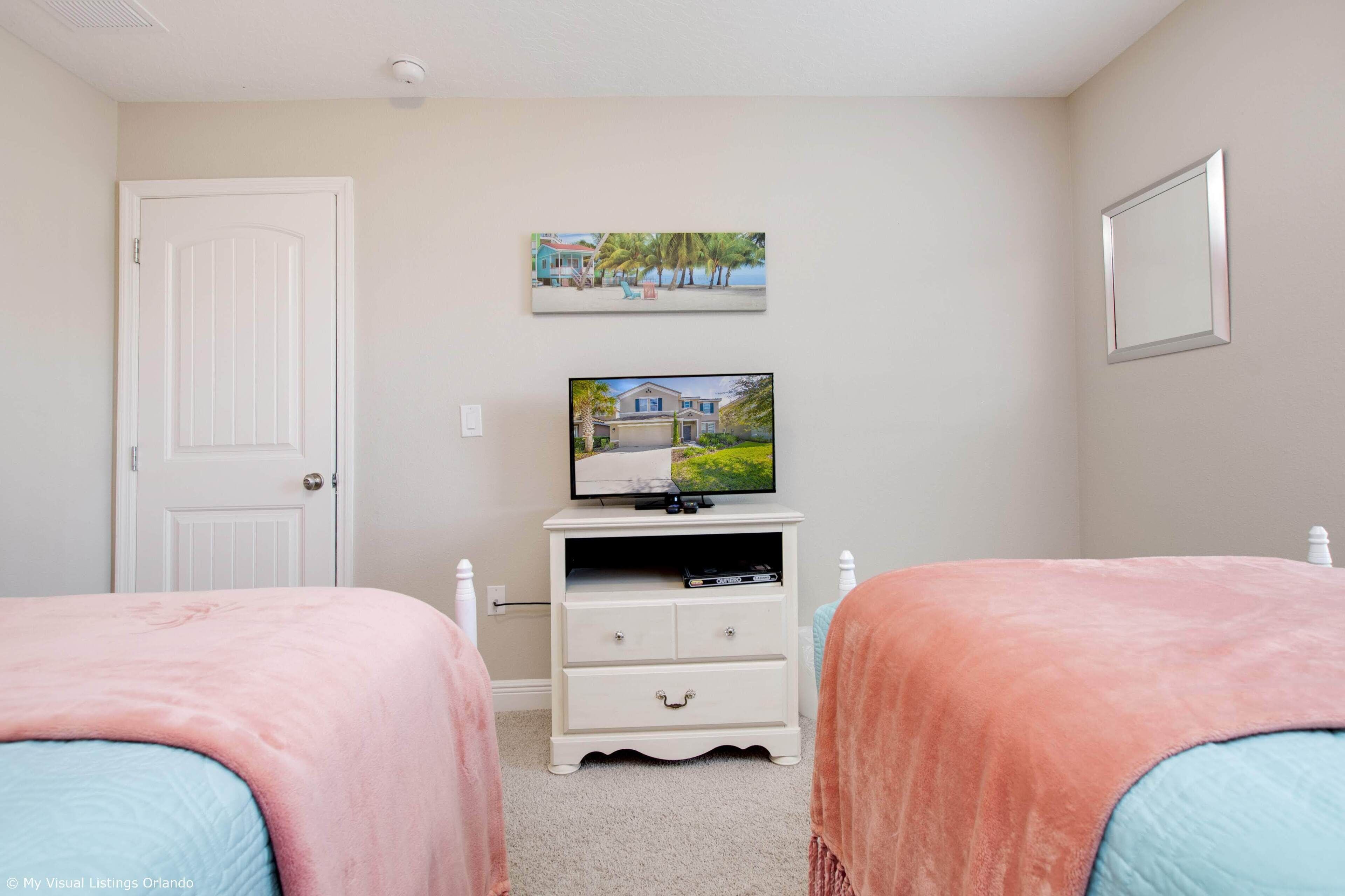 A bedroom with two beds, a television on a dresser, and a door.
