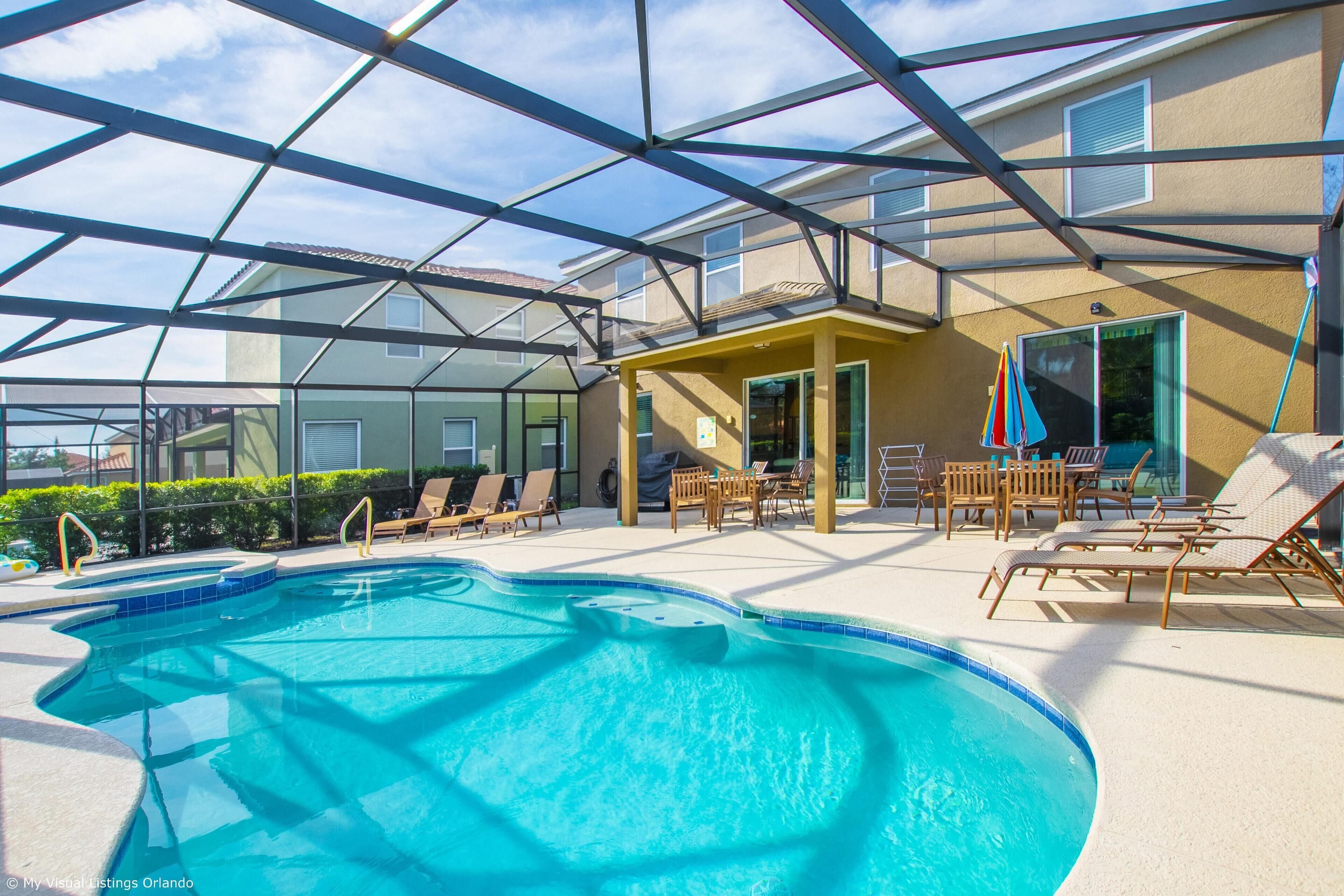 A swimming pool with a glass roof, surrounded by lounge chairs and a covered patio area.