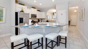 A modern kitchen with white cabinets, a central island with bar stools, stainless steel appliances, and a herringbone tile floor.