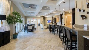 A hotel lobby with a reception desk, bar area, seating, and a large potted plant.