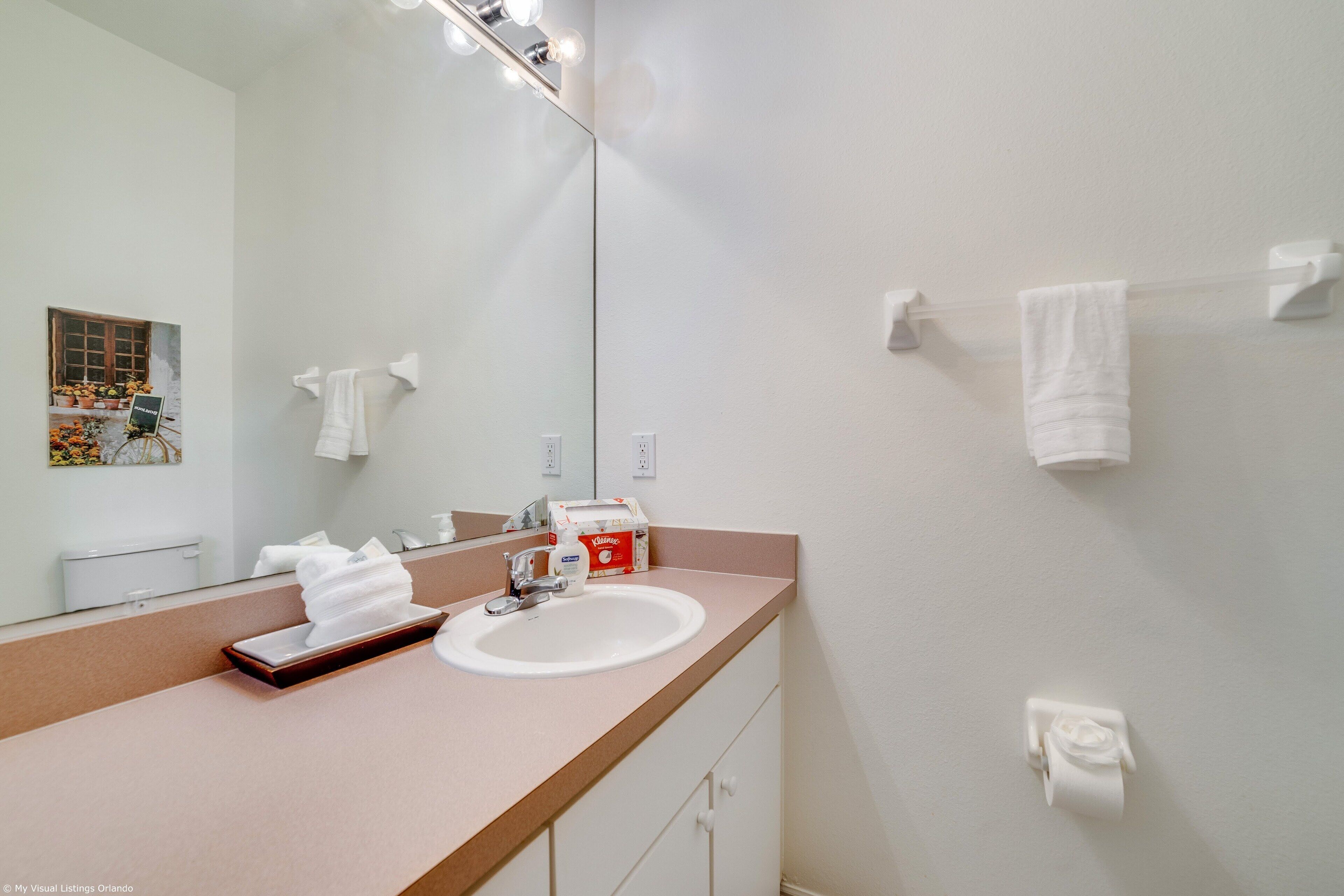 A modern bathroom with a large mirror, white sink, and towel rack.